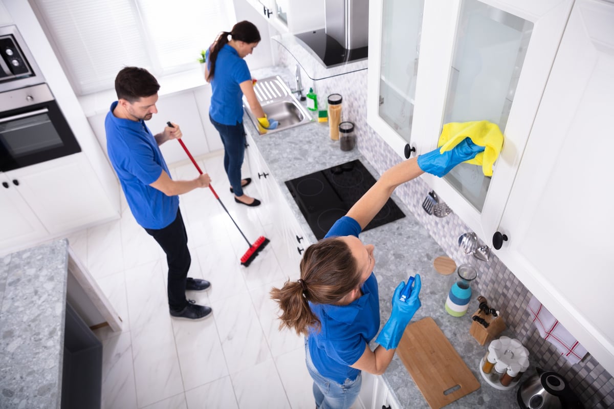 Group Of Young Janitors In Uniform Cleaning Kitchen At Home