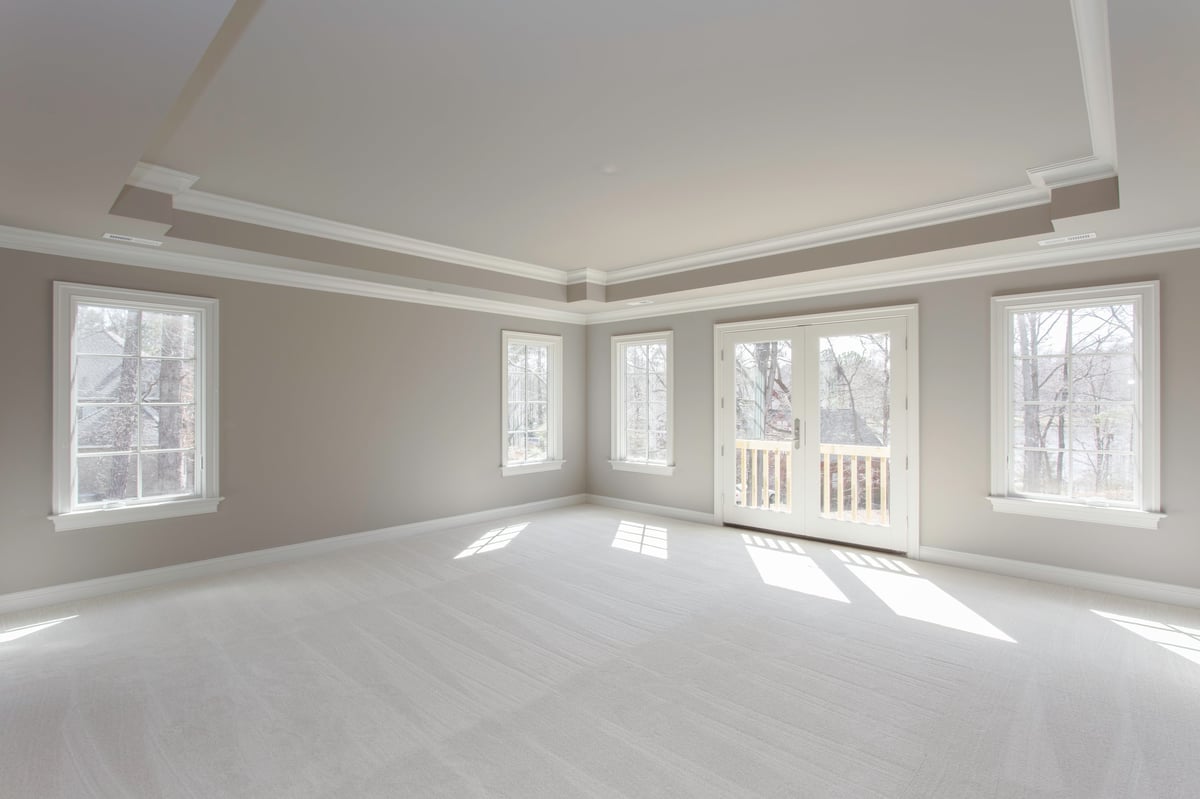 An expansive, empty room with soft carpeting, neutral walls, and large windows letting in natural light, creating a bright and inviting blank canvas for decorating