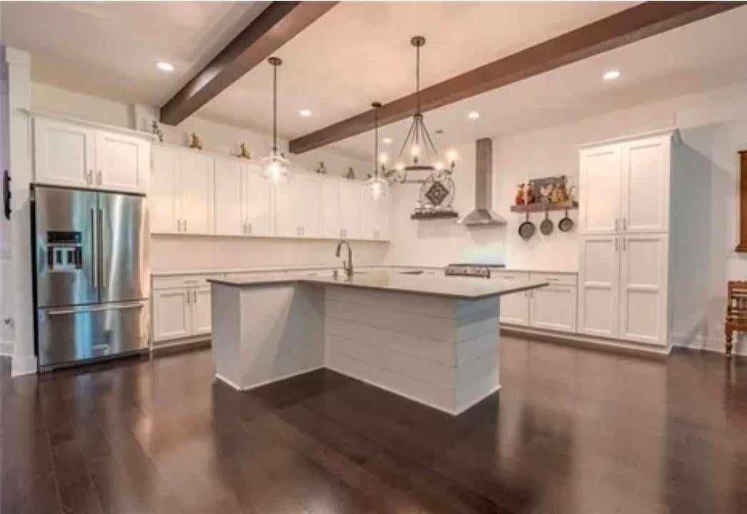 Modern kitchen with white cabinetry, large island, stainless steel appliances, wooden beams, and dark hardwood floors