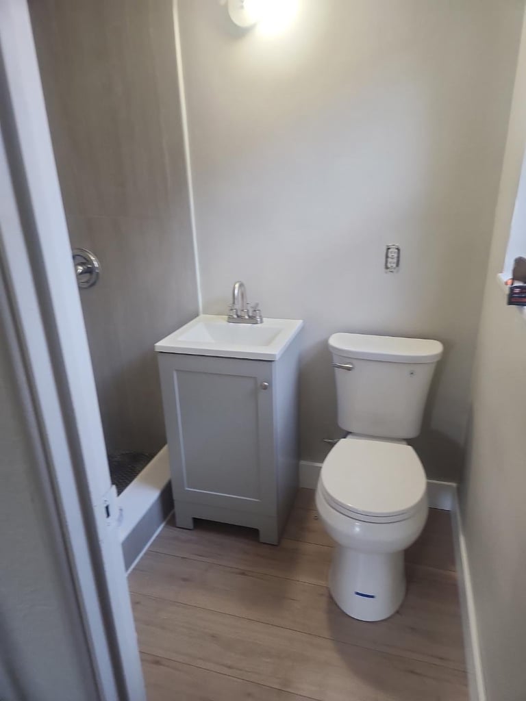 Small bathroom interior with white toilet, pedestal sink, wood-look flooring, and overhead lighting in a compact space
