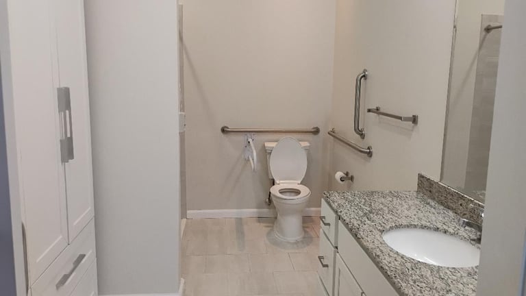 Modern bathroom with toilet, white vanity sink with granite countertop, grab bars, and tile flooring