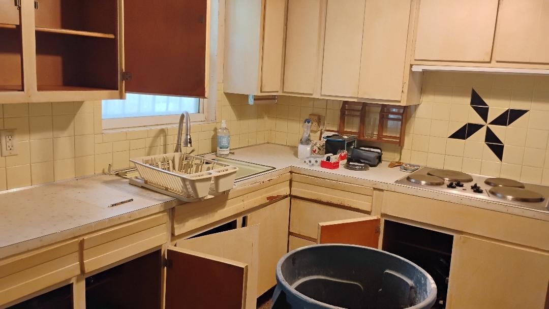 Vintage kitchen with light wood cabinets, cream subway tile backsplash, countertops with sink and stove, and a large black pot on the floor