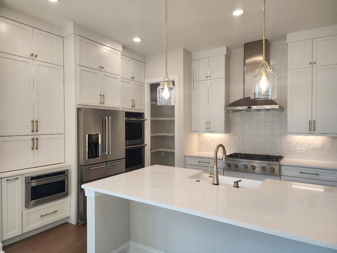 Modern kitchen with white cabinetry, stainless steel appliances, white quartz countertop island, and recessed lighting