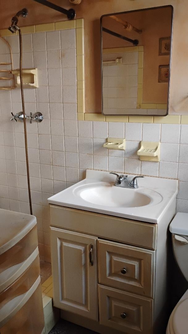 Vintage bathroom with beige and white tile walls, pedestal sink with cabinet, framed mirror, shower area, and toilet