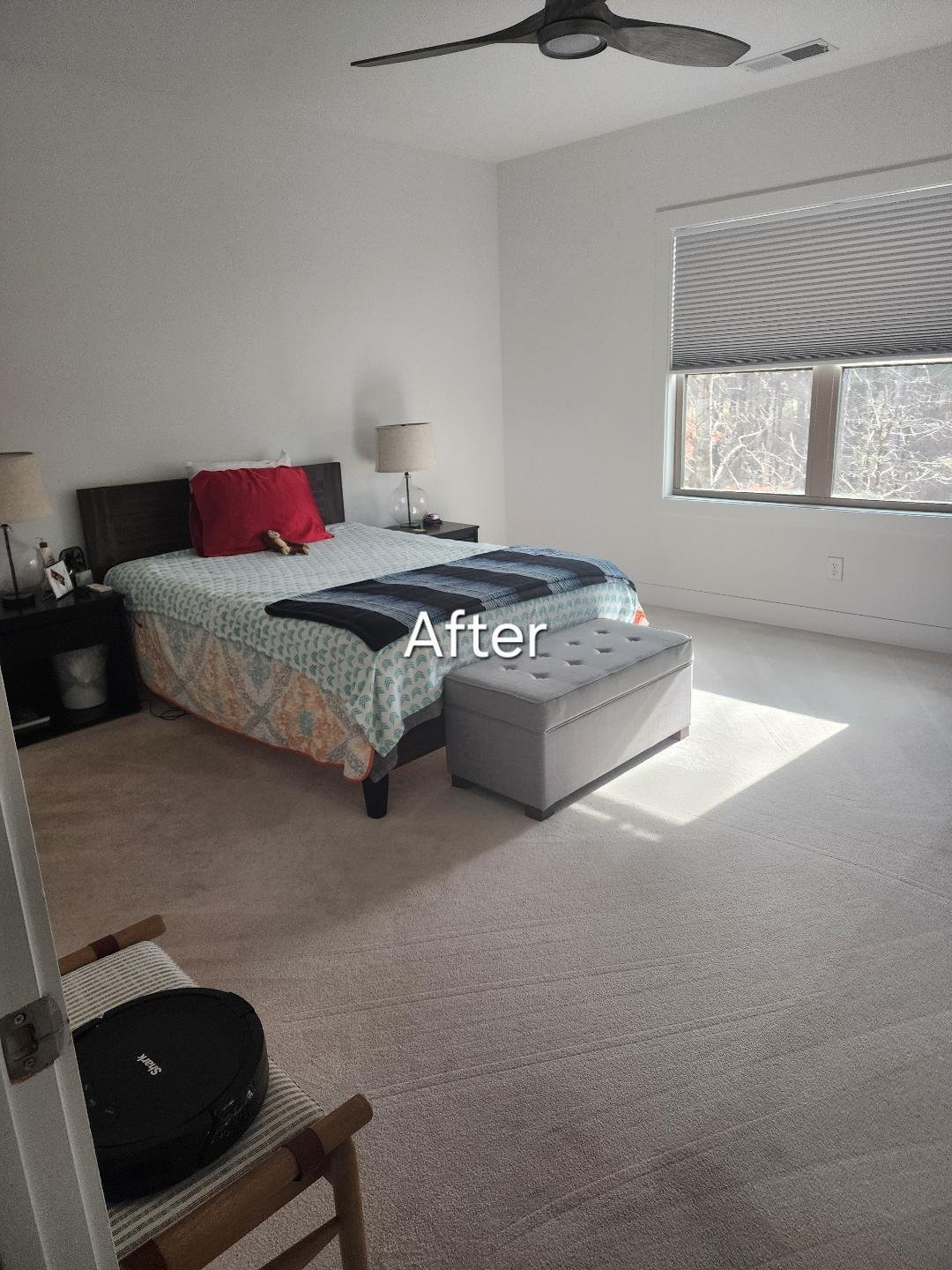 Bright bedroom interior labeled After showing a bed with red pillow, gray ottoman, ceiling fan, window with blinds, and neutral carpet flooring