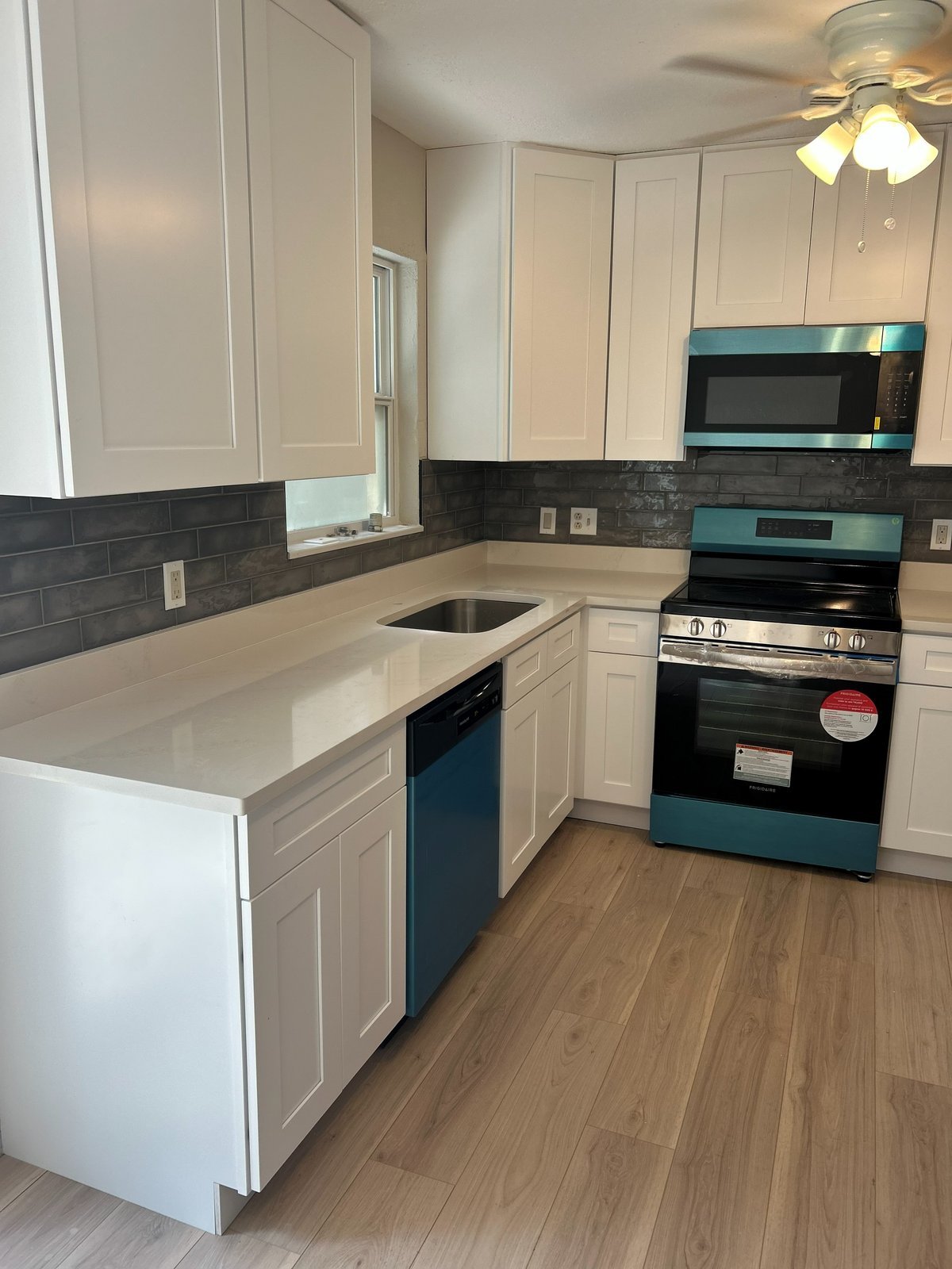Modern kitchen with white cabinets, turquoise appliances, dark tile backsplash, white countertops, and wood-look flooring