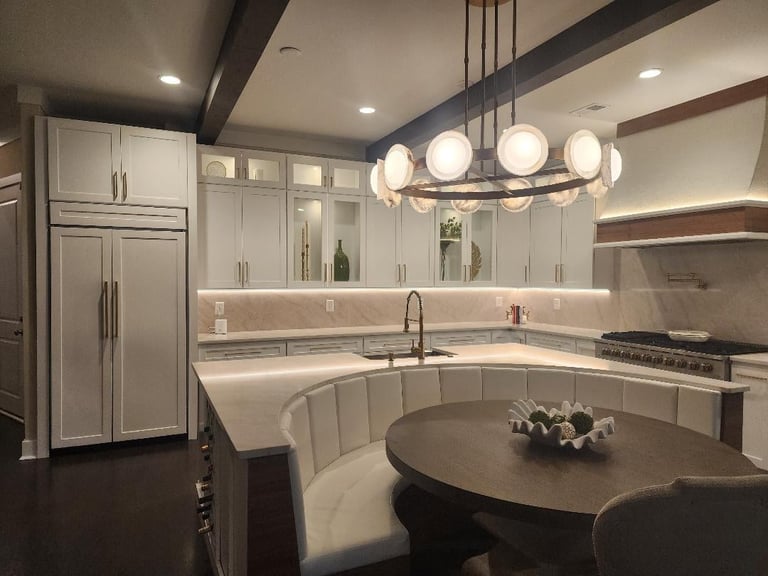 Modern kitchen with white cabinetry, curved white seating, dark round table, pendant lighting, and stainless steel appliances