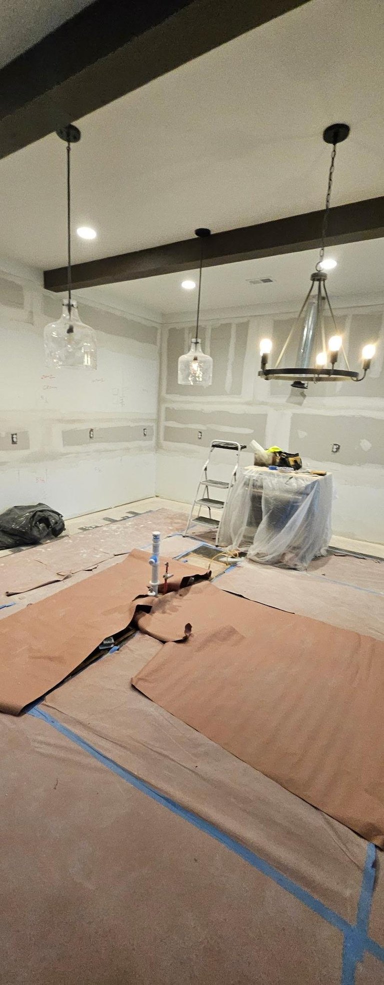 Kitchen renovation in progress with white subway tile backsplash, two pendant lights hanging from dark beam, and construction materials on floor