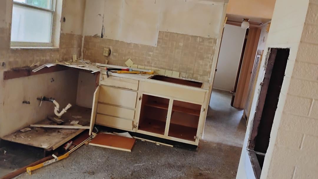 Abandoned kitchen with gutted cabinets, open drawers, and damaged countertops in a deteriorating interior space
