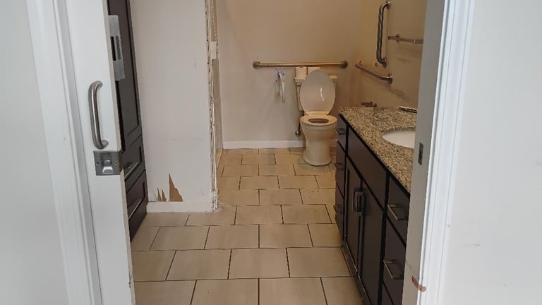 Bathroom interior with beige tile flooring, dark vanity cabinets, toilet, and shower stall with grab bars